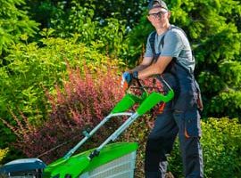A man standing next to a green lawn mower.