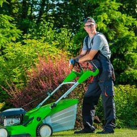 A man standing next to a green lawn mower.