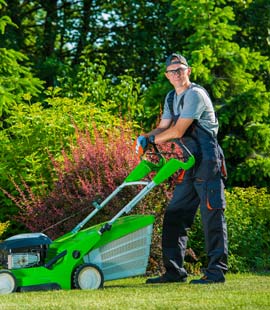 A man standing next to a green lawn mower.