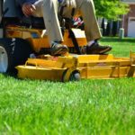 A man riding on the back of a yellow lawn mower.