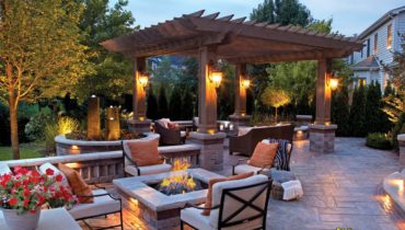 A patio with fire pit and pergola at night.